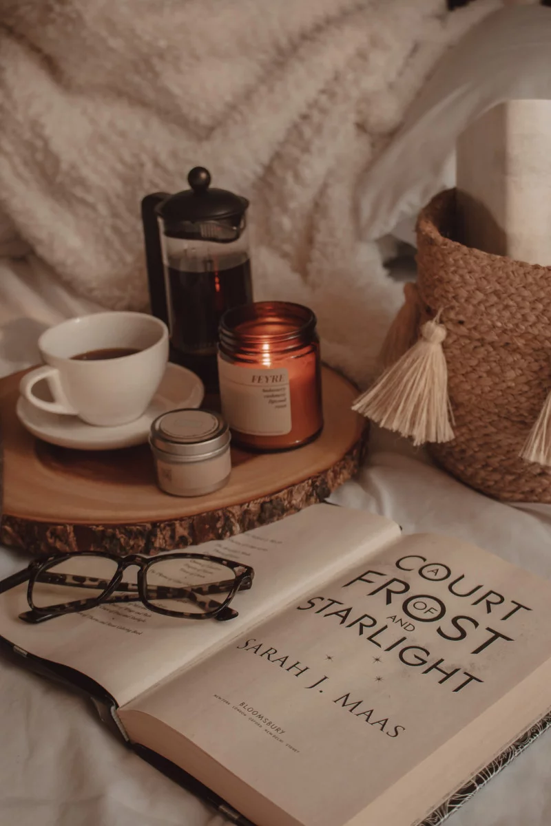 a court of frost and starlight book opened with glasses resting on top next to mug of coffee and burning candle