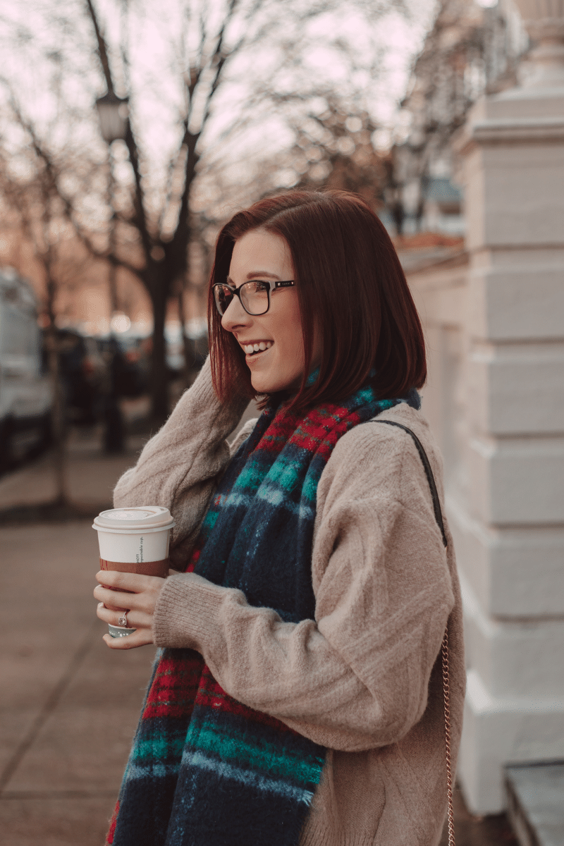 girl holding coffee with plaid scarf and taupe sweater