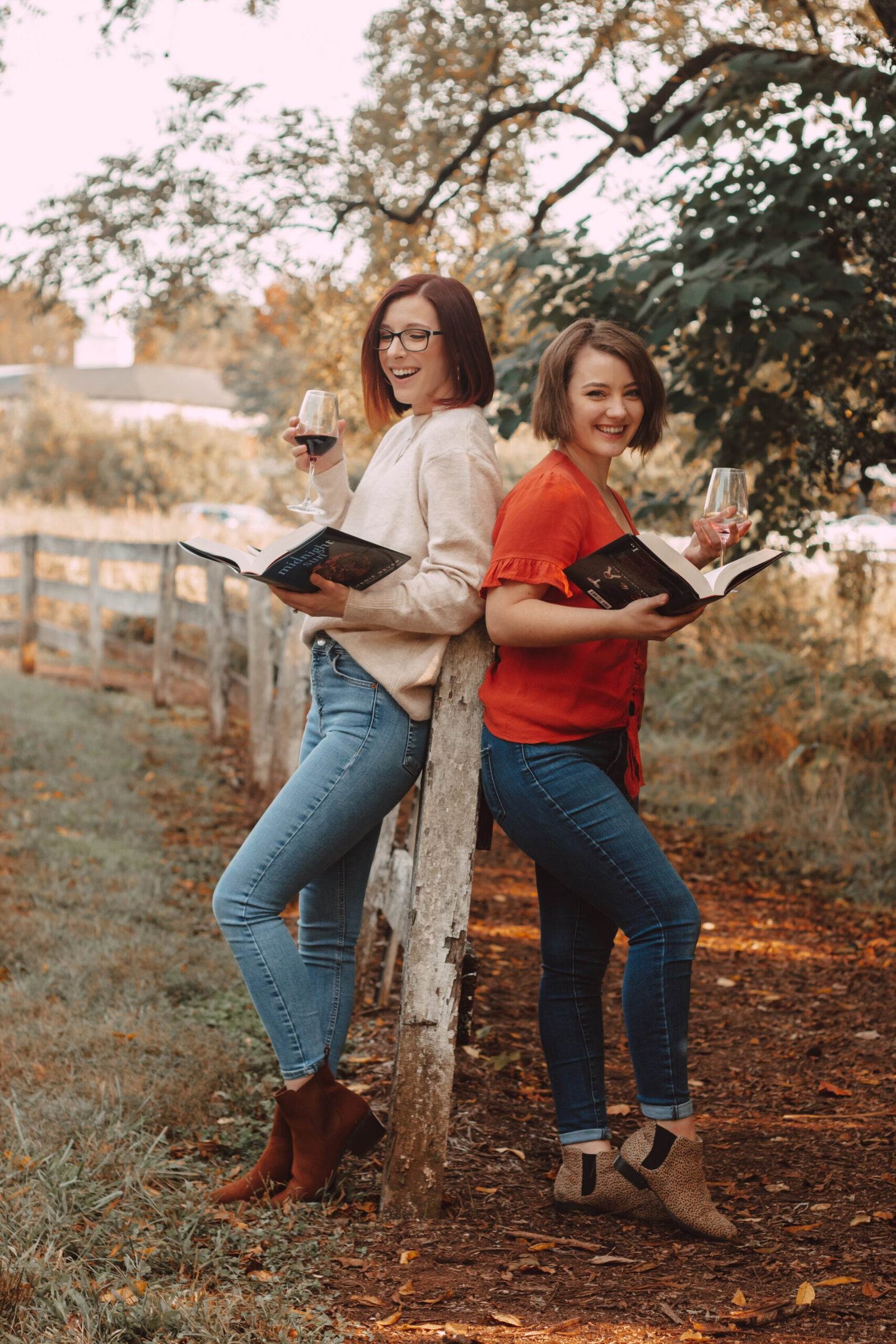 two girls holding midnight sun and sipping wine by a fence