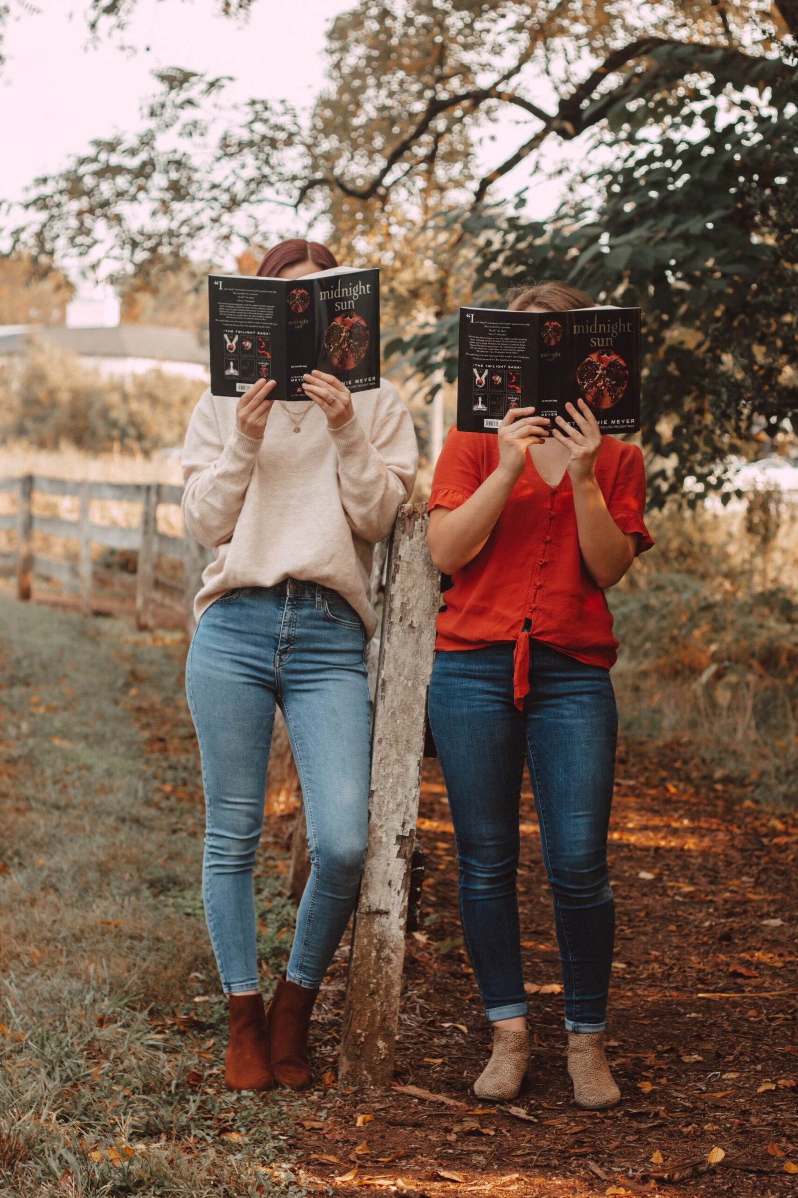 two girls holding midnight sun in front of their faces by a fence