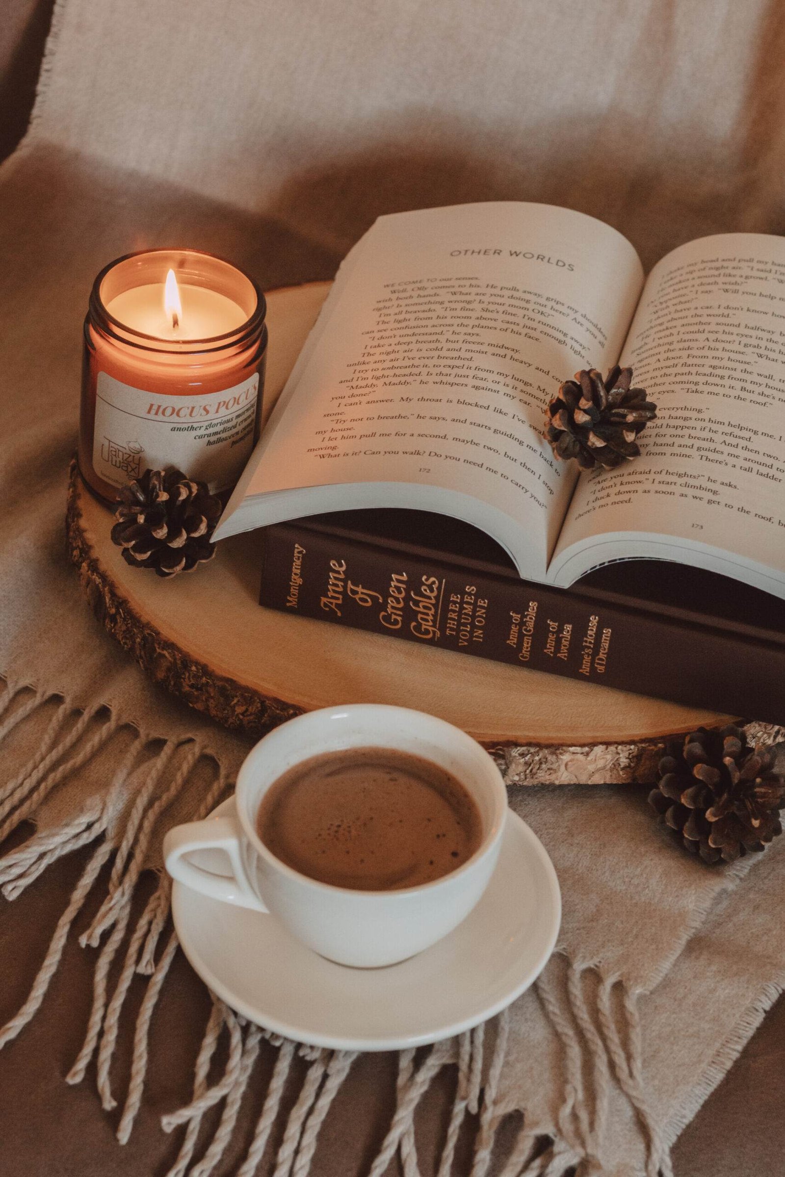 mug of swirling mocha sitting next to two books on top of a wooden board next to a lit candle