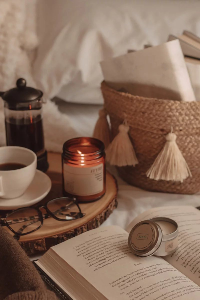 candle burning next to mug of coffee and glasses with a small candle on top of a book