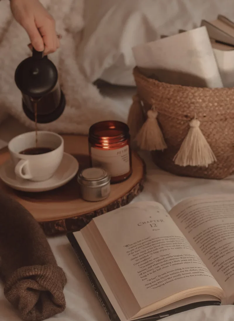 book opened next to a couple of candles and coffee being poured into a mug