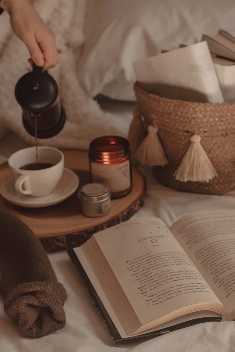 book opened next to a couple of candles and coffee being poured into a mug