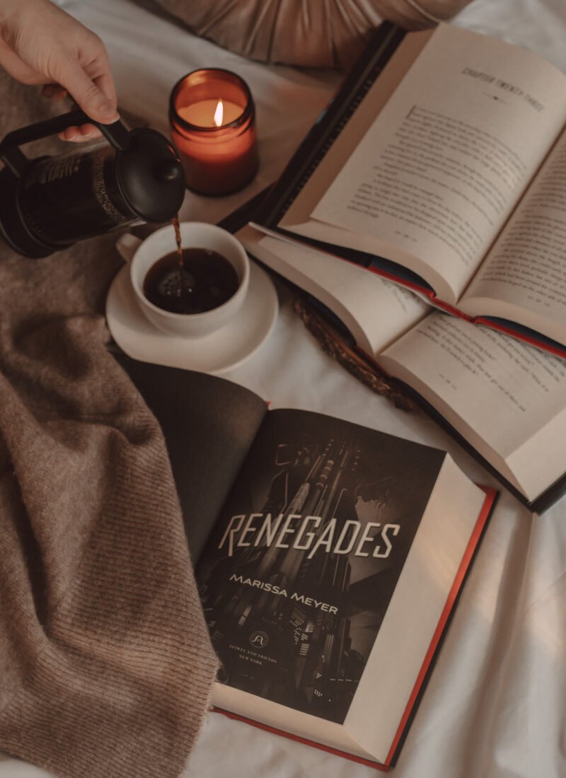 Renegades book title page open next to two other books stacked on top of one another and a hand pouring coffee into a mug
