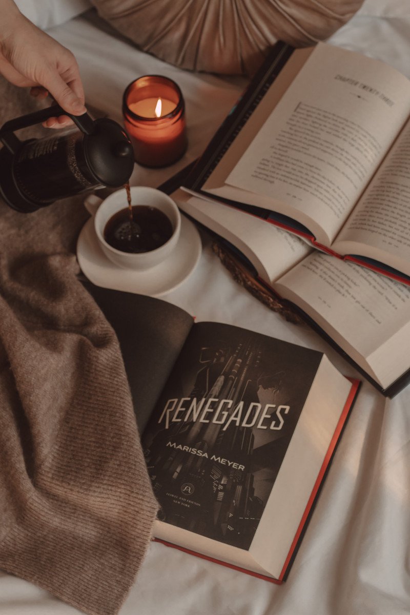 Renegades book title page open next to two other books stacked on top of one another and a hand pouring coffee into a mug