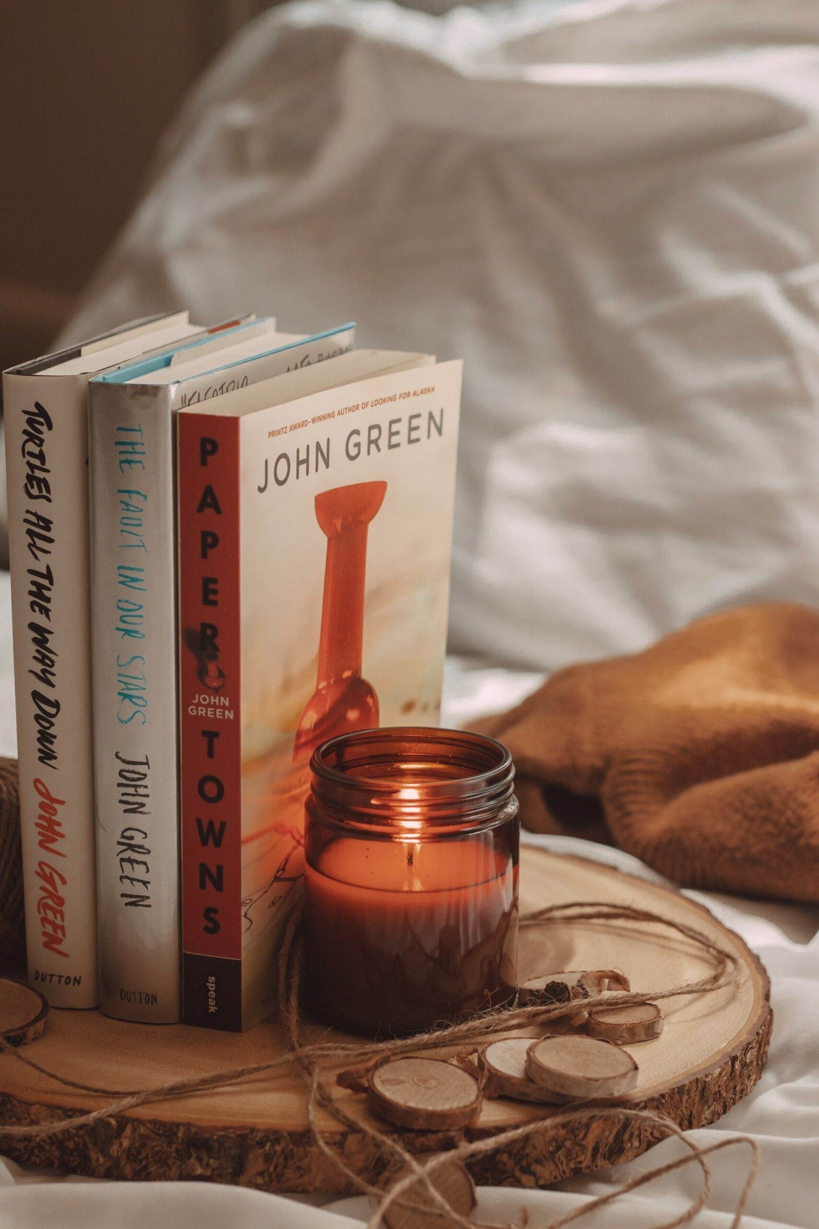 paper towns, the fault in our stars, and turtles all the way down books by john green next to a lit candle