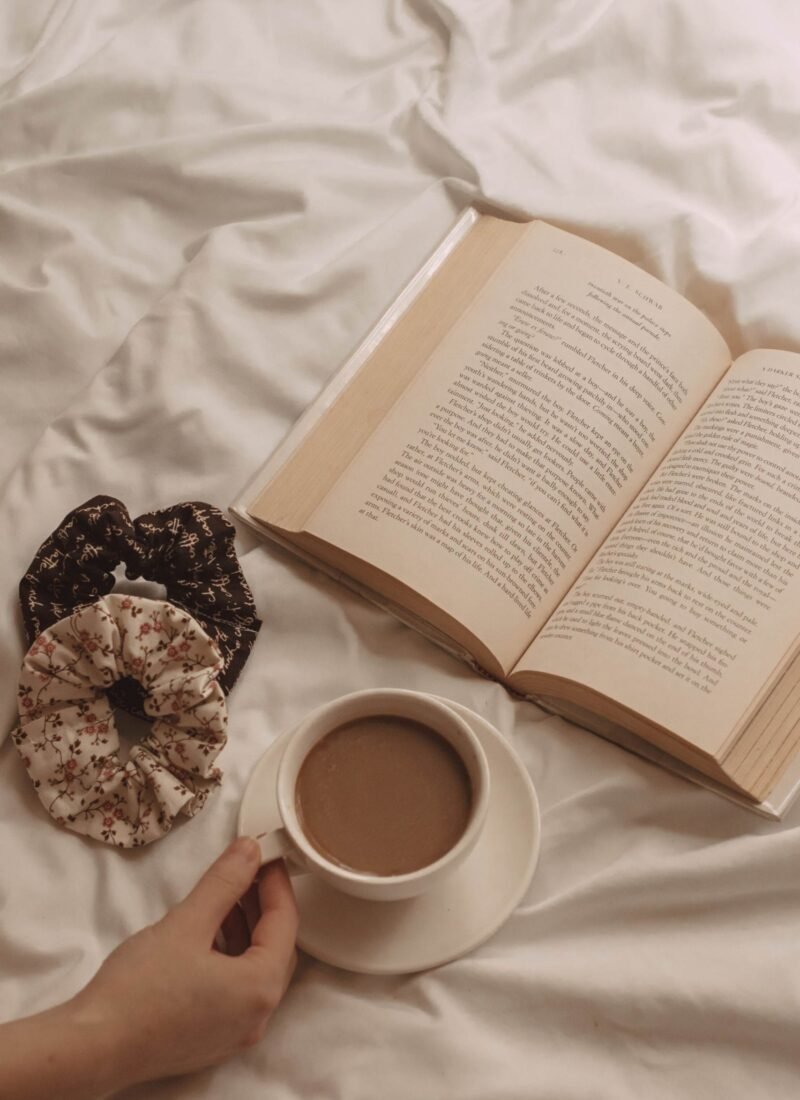 hand holding a mug of coffee next to and open book and hair scrunchies