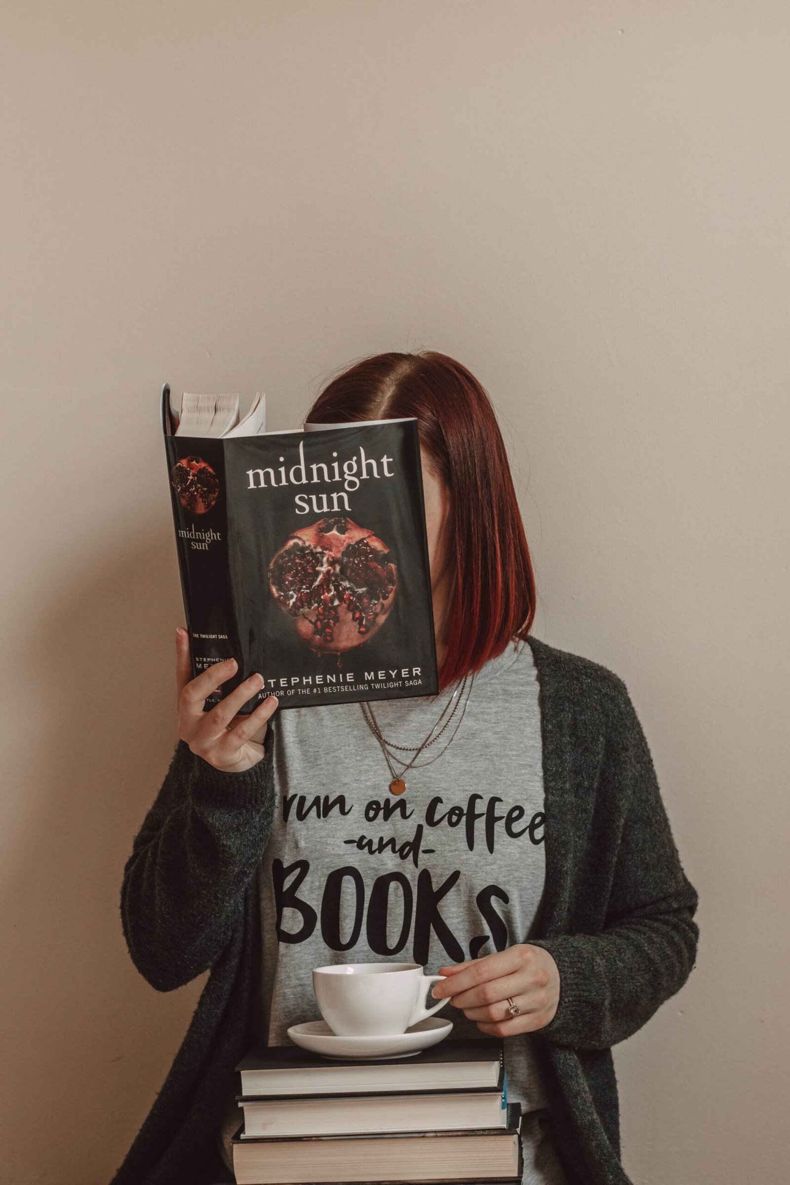 girl holding midnight sun book in front of her face while wearing a shirt that says "i run on coffee and books"